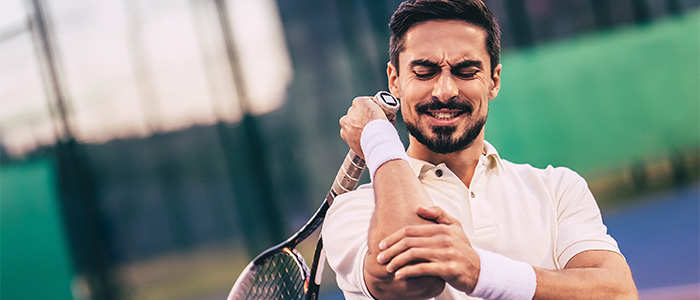 man holding elbow in pain while on tennis courst